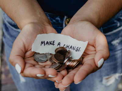 Close-up of a person holding coins and a piece of paper that says 'Make a Change' in their cupped hands.